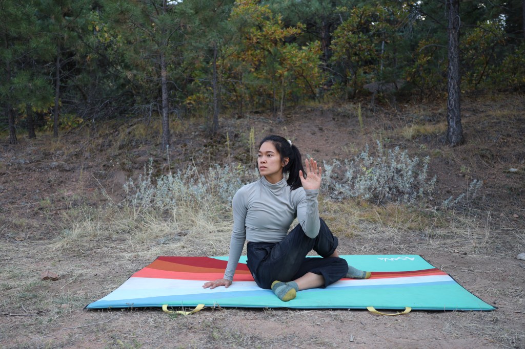 A woman doing outdoor yoga in the pose half lord of the fishes, a deep spinal twist, surrounded by trees and plants.