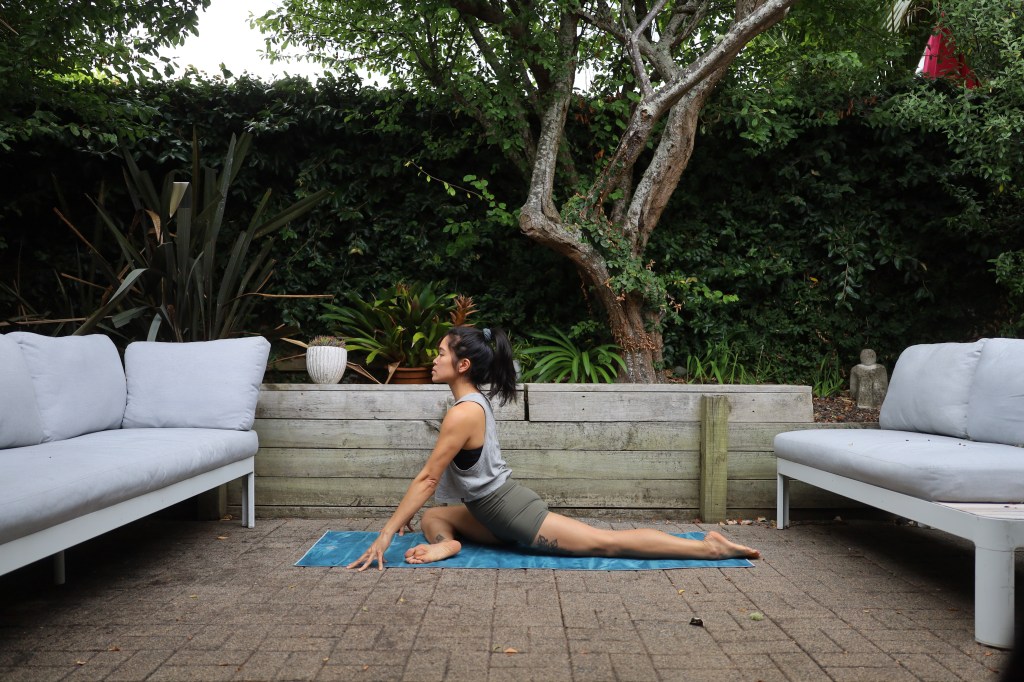 A woman in the yoga pose half pigeon in a backyard patio